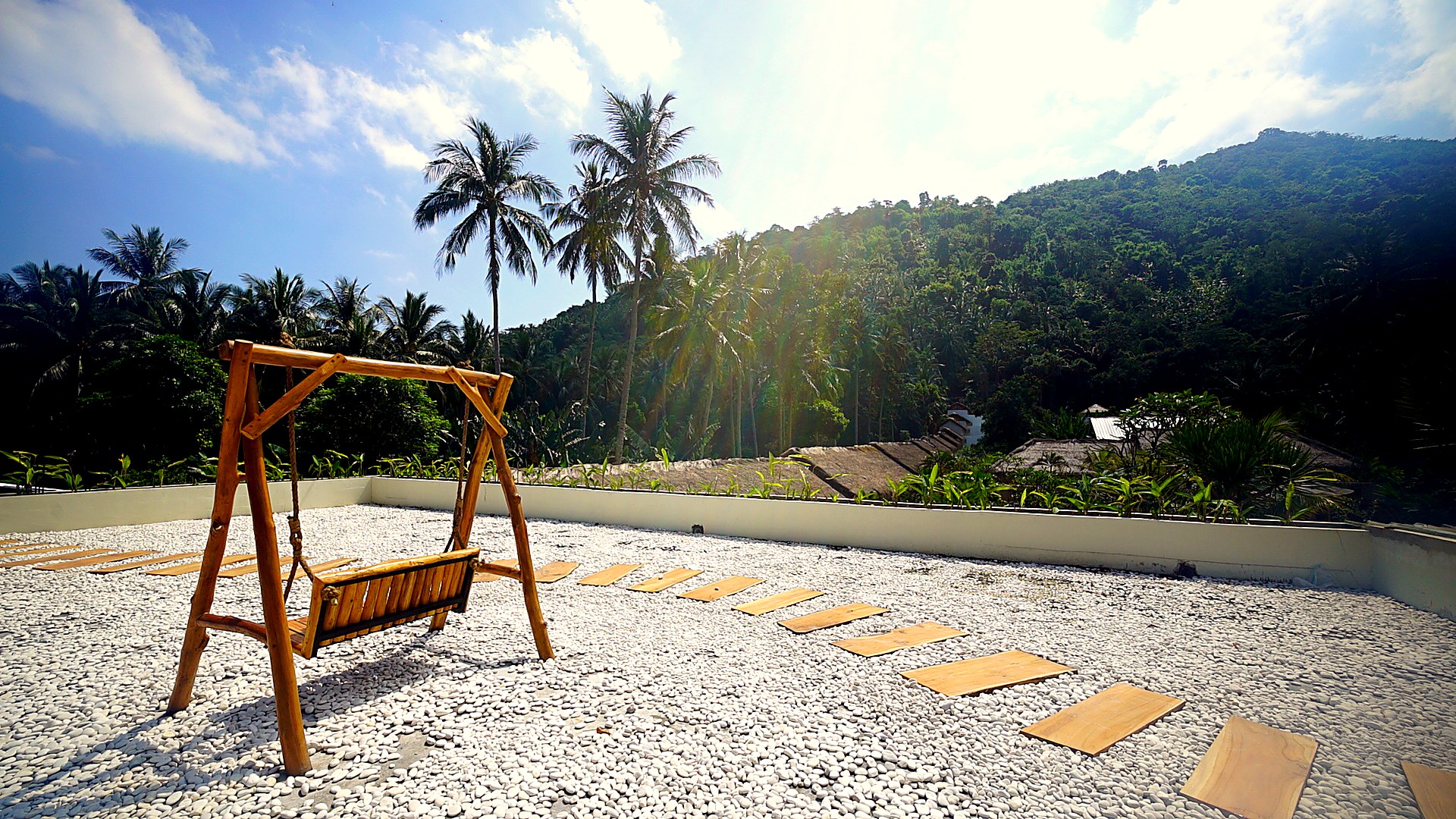 Bamboo swing on a white-pebble rooftop terrace with palm trees and jungle backdrop