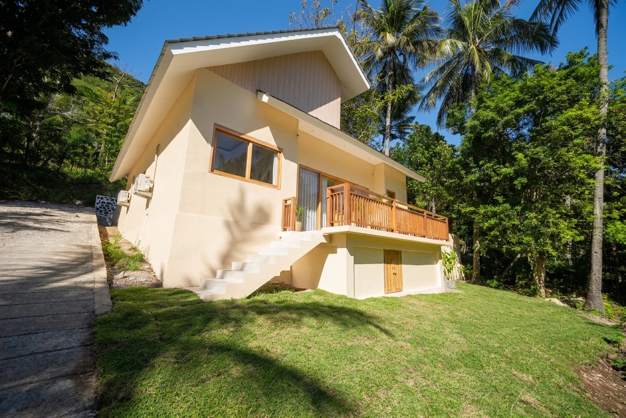 Standalone two-storey villa facade with wooden terrace and tropical garden