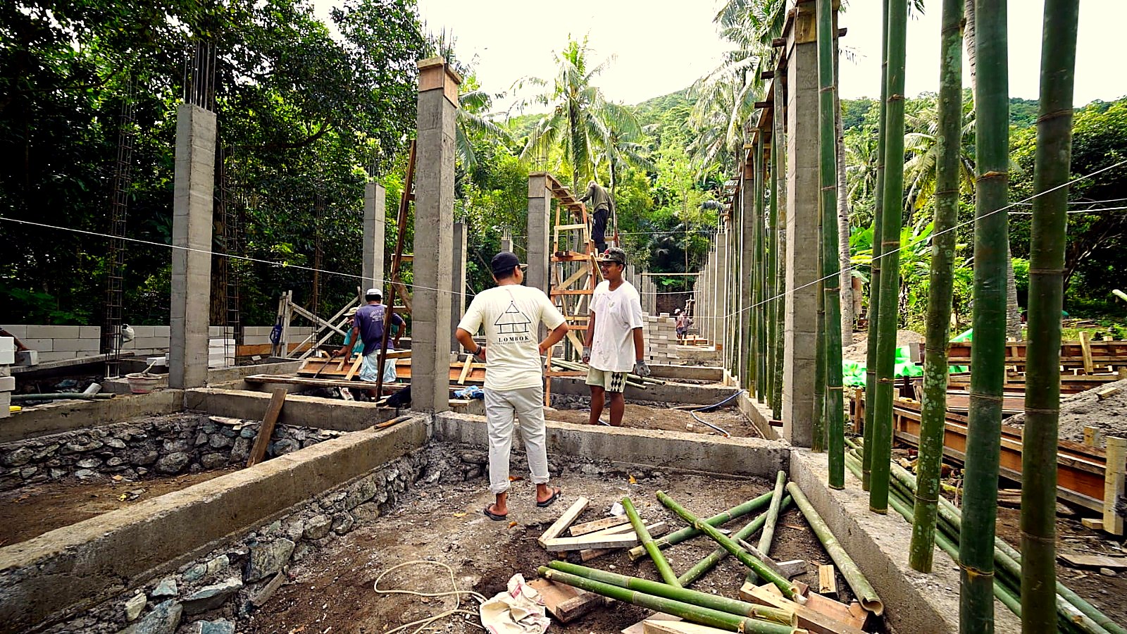 Wide view of the build: concrete columns, palm trees and crew working on formwork