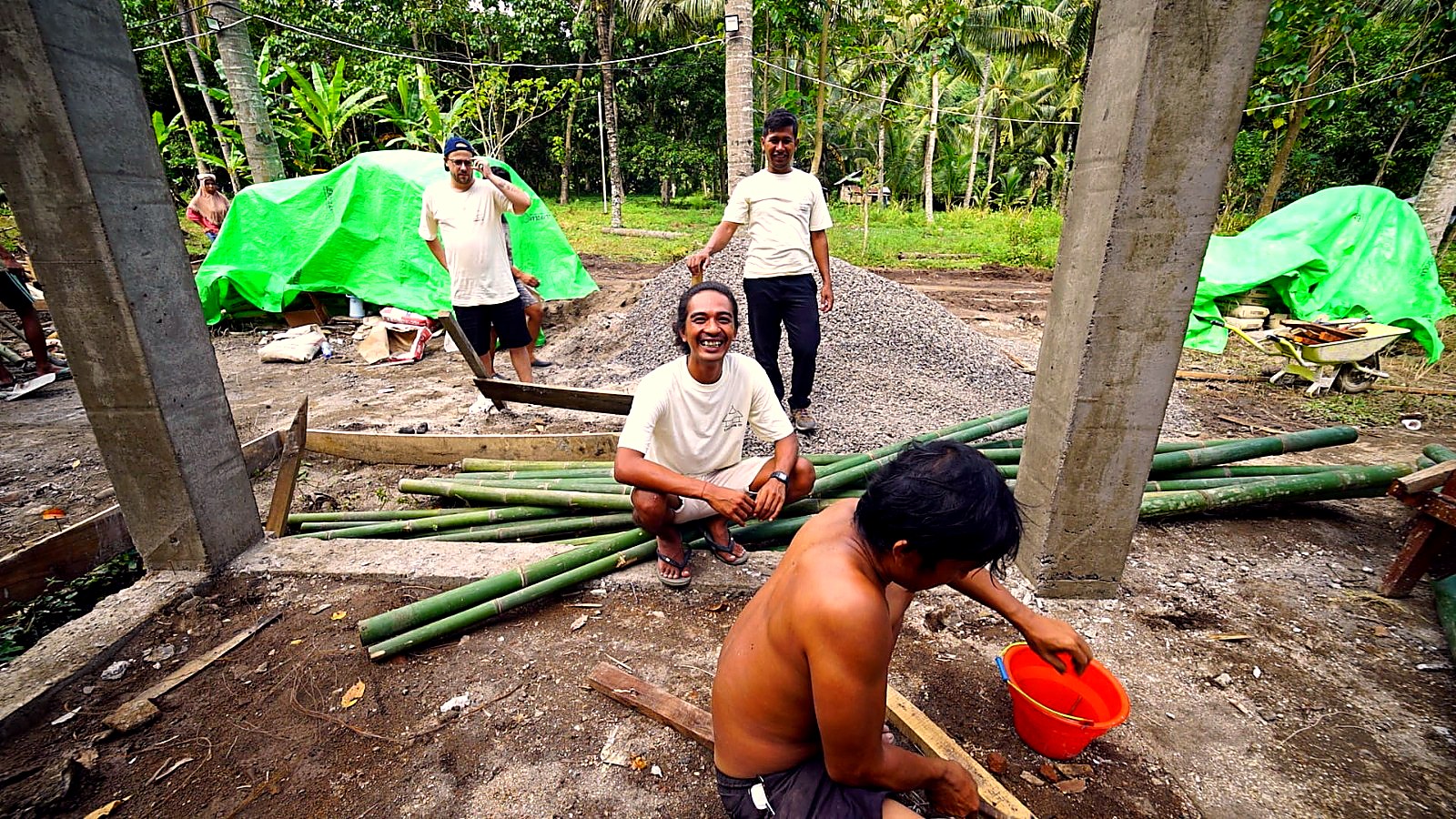 Four crew members smiling on site beside bamboo bundles and gravel piles