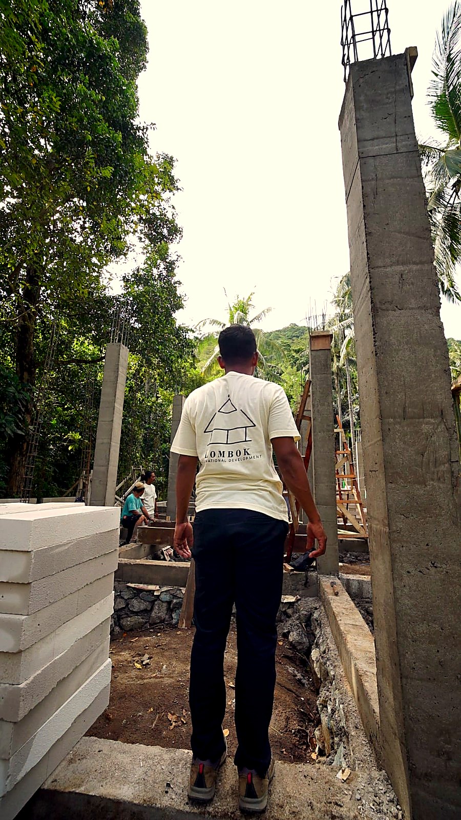 Worker seen from behind wearing the Lombok International Development T-shirt among the concrete columns